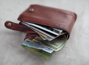 we see a brown leather wallet over packed with different currency and credit cards on a pale marble surface