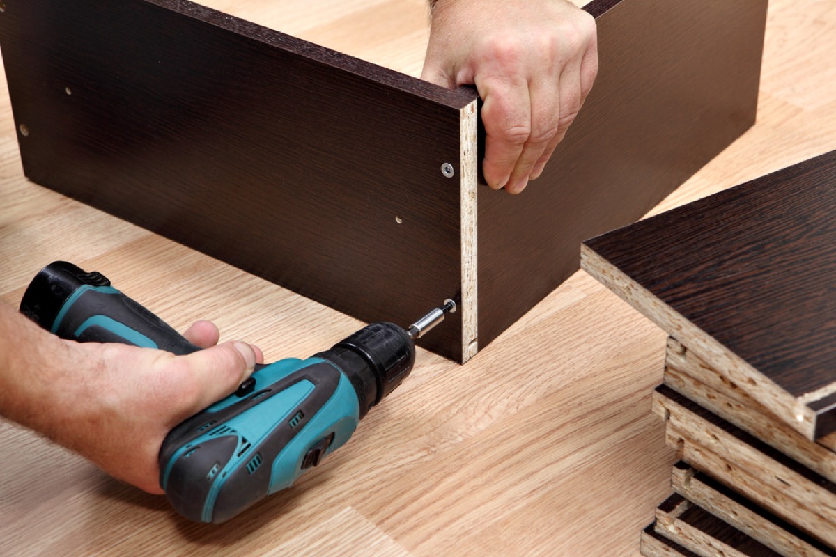 man drilling together black particleboard furniture, home upgrades