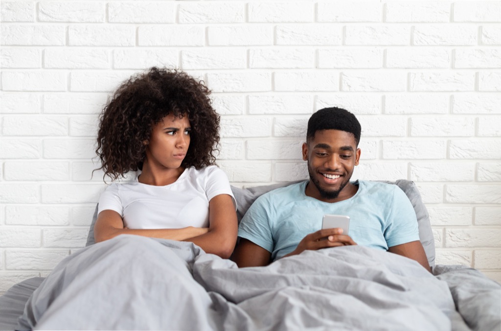 man texting in bed with a woman