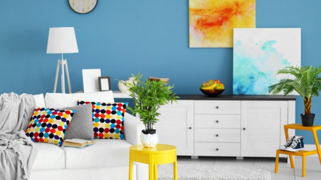 trendy home interior with white furniture and floors, yellow and blue art, blue wall with clock, and white lamp