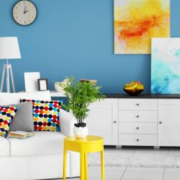 trendy home interior with white furniture and floors, yellow and blue art, blue wall with clock, and white lamp