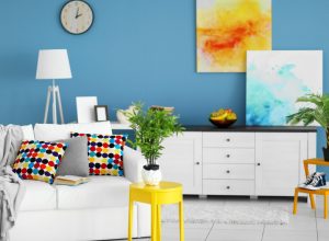 trendy home interior with white furniture and floors, yellow and blue art, blue wall with clock, and white lamp