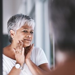 Mature woman touching her face with her hands while looking at her reflection in a mirror