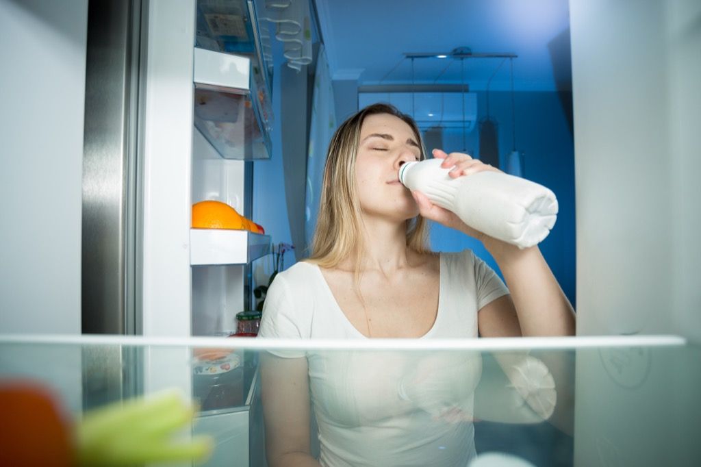 woman drinking milk from a fridge