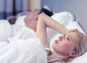 woman lying awake at night in bed with sleeping husband
