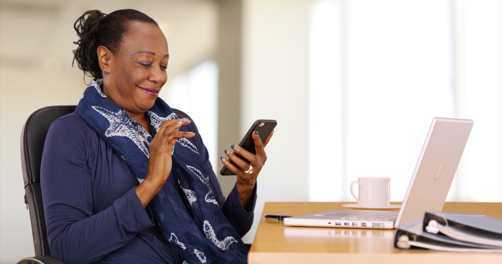 older black woman texts on phone at desk to talk to customer service rep