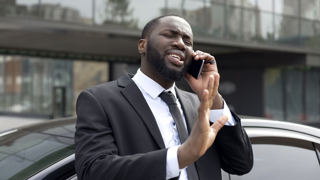 frustrated black man in suit talks on Phone, trying to reach customer service rep