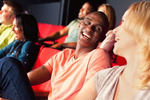 ชายแอฟริกันอเมริกันยิ้มและหัวเราะขณะชมภาพยนตร์หรือรายการกับแฟนสาว