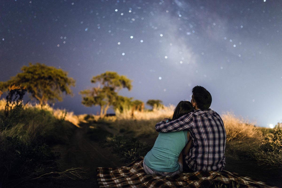 couple embrace on picnic blanket under the stars