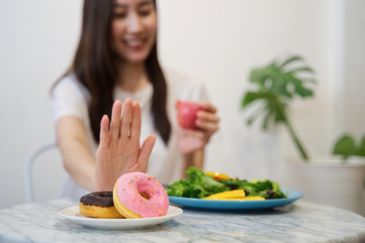 young woman with a plate of salad in front of her pushing away a plate of donuts