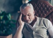 man sitting in an armchair suffering from a headache - what causes headaches