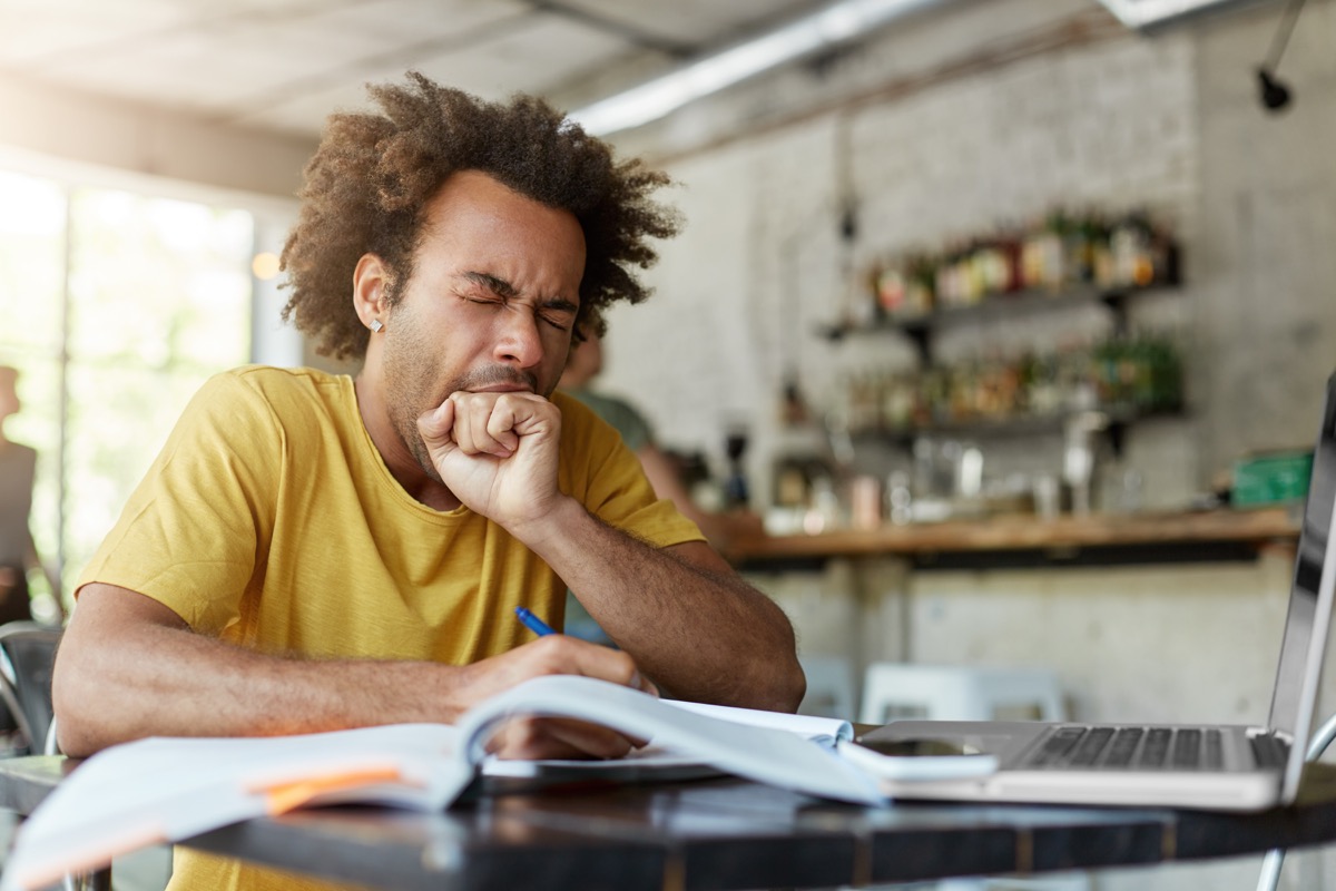 man doing work at a kitchen table and yawning lies over 40
