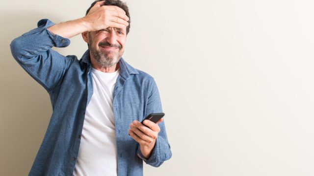 middle aged man using smartphone stressed with hand on head