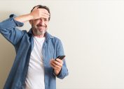 middle aged man using smartphone stressed with hand on head