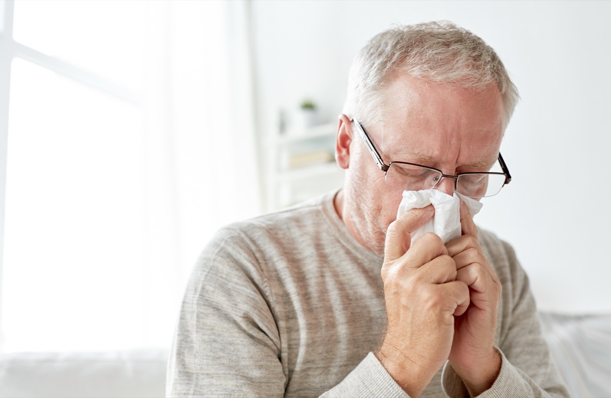 Older man with a cold blowing his nose into a tissue