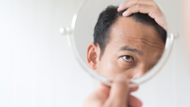 older man looking in mirror at hair loss, over 50 regrets