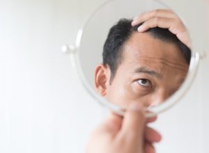 older man looking in mirror at hair loss, over 50 regrets