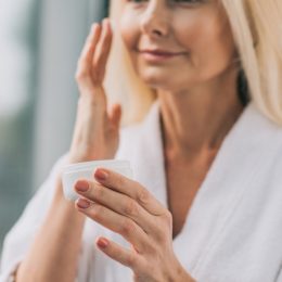 mature woman applying face cream in white robe