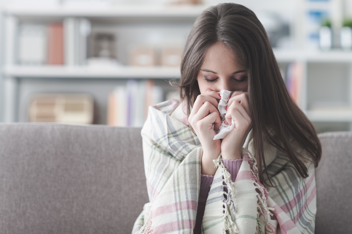 woman blowing her nose on the couch {Allergy Symptoms}