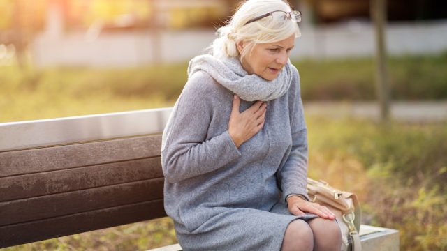 older woman sits on bench clutching chest, what your indigestion means