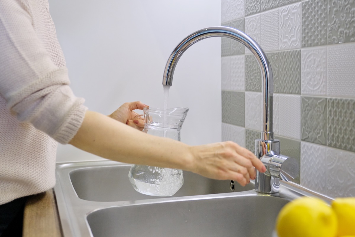 Woman filling a carafe with water form the kitchen sink