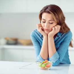middle aged woman looks disappointed at small salad while standing in kitchen