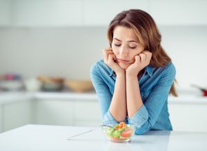 middle aged woman looks disappointed at small salad while standing in kitchen