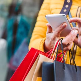 closeup of shopper in yellow coat with bags and phone in hand