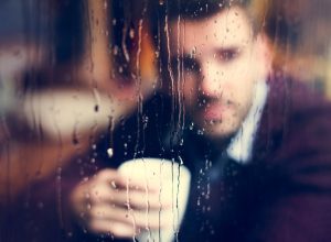 contemplative man holding a cup of coffee looking out a rainy window {stereotypes}