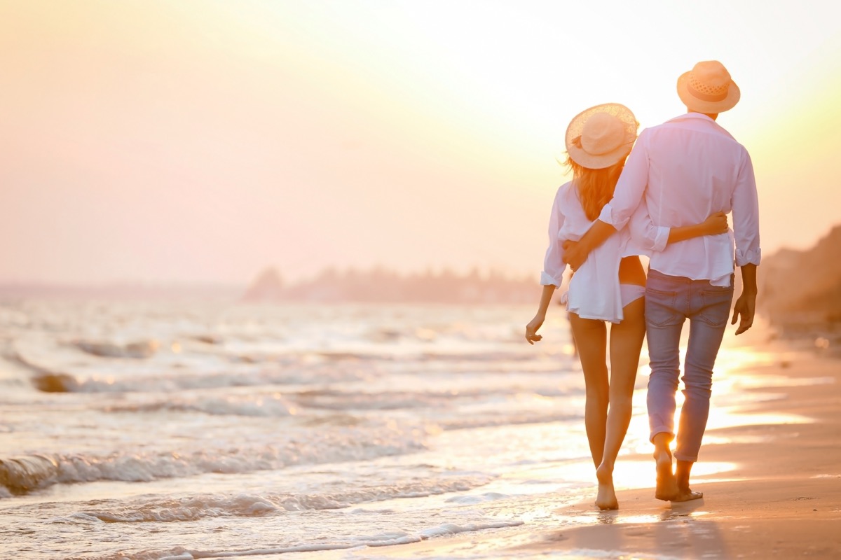 couple wearing hats walking on a beach at sunset - money can't buy happiness