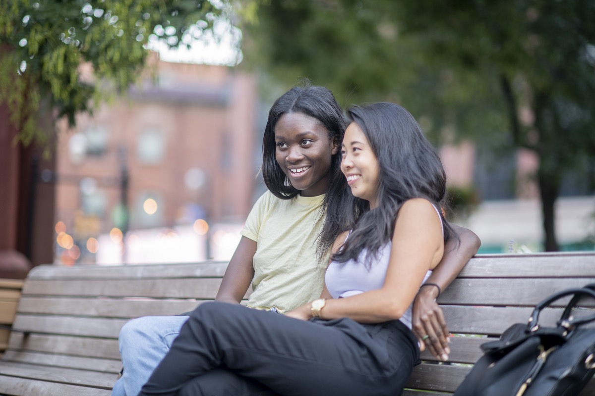 An interracial couple is siting on a park bench. They are embracing and enjoying the day.