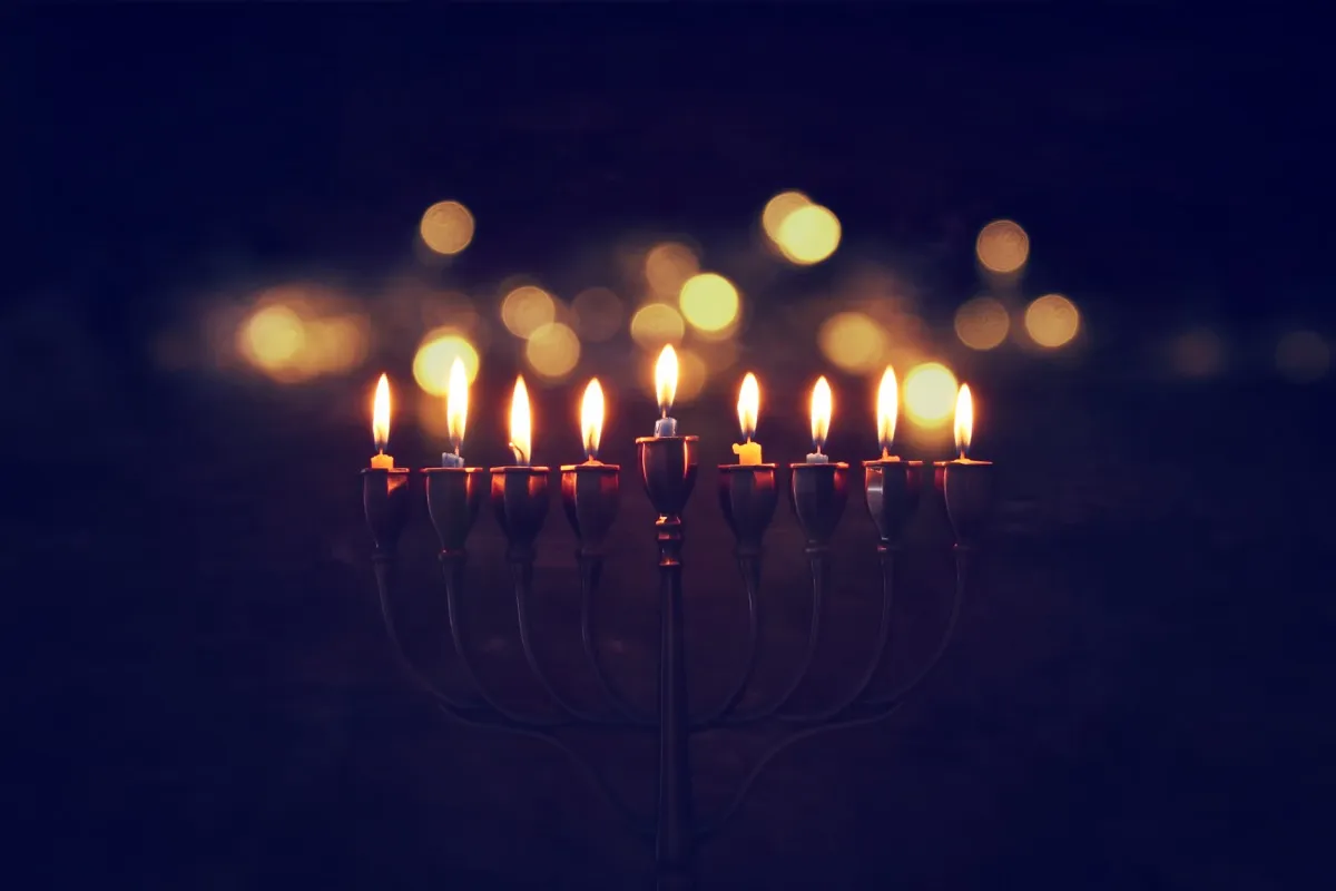 a lit menorah in darkness - hanukkah traditions