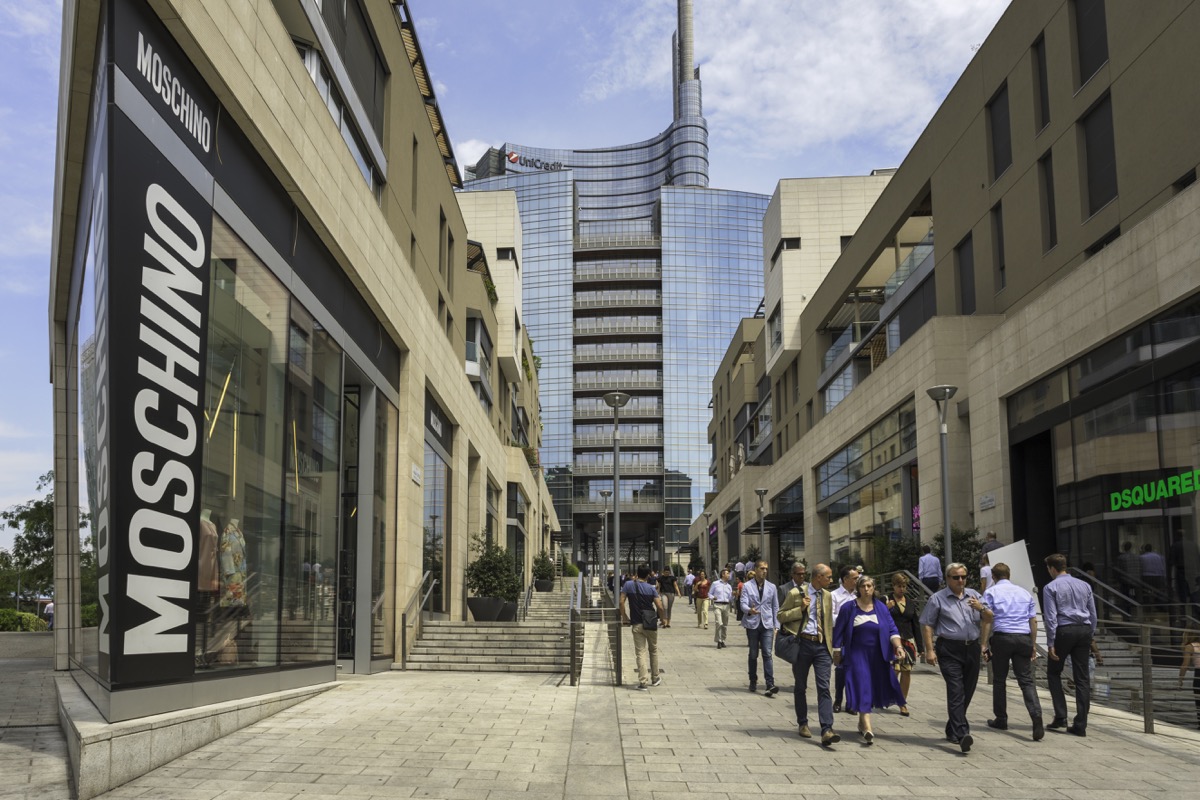 People walking down a street lined with stores and restaurants in the modern Porta Nuova district of Milan.