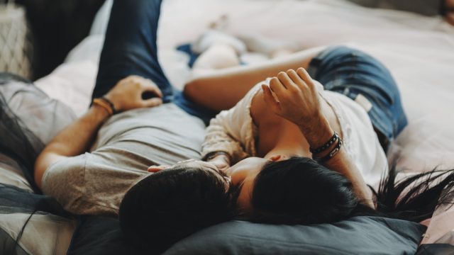 attractive romantic couple laying on bed ,hugging and kissing in a cozy room.