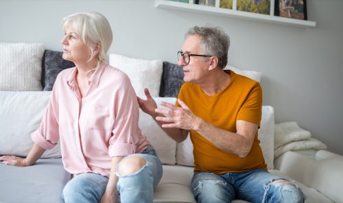Senior man arguing with his wife who has her back turned to him as they sit on the couch