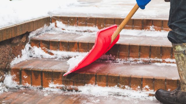 person shoveling snow on brick steps with red shovel