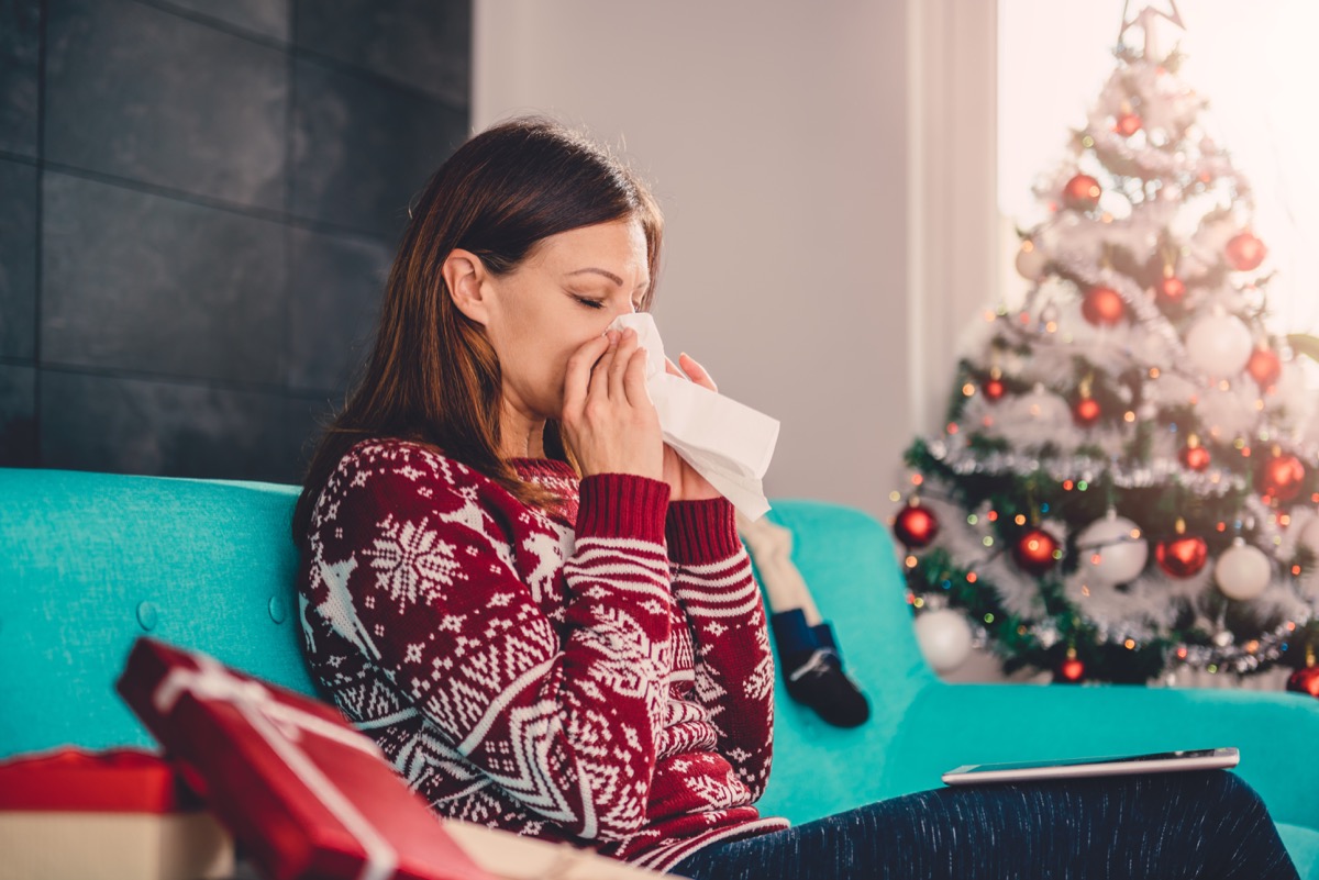 woman blowing her nose next to christmas tree