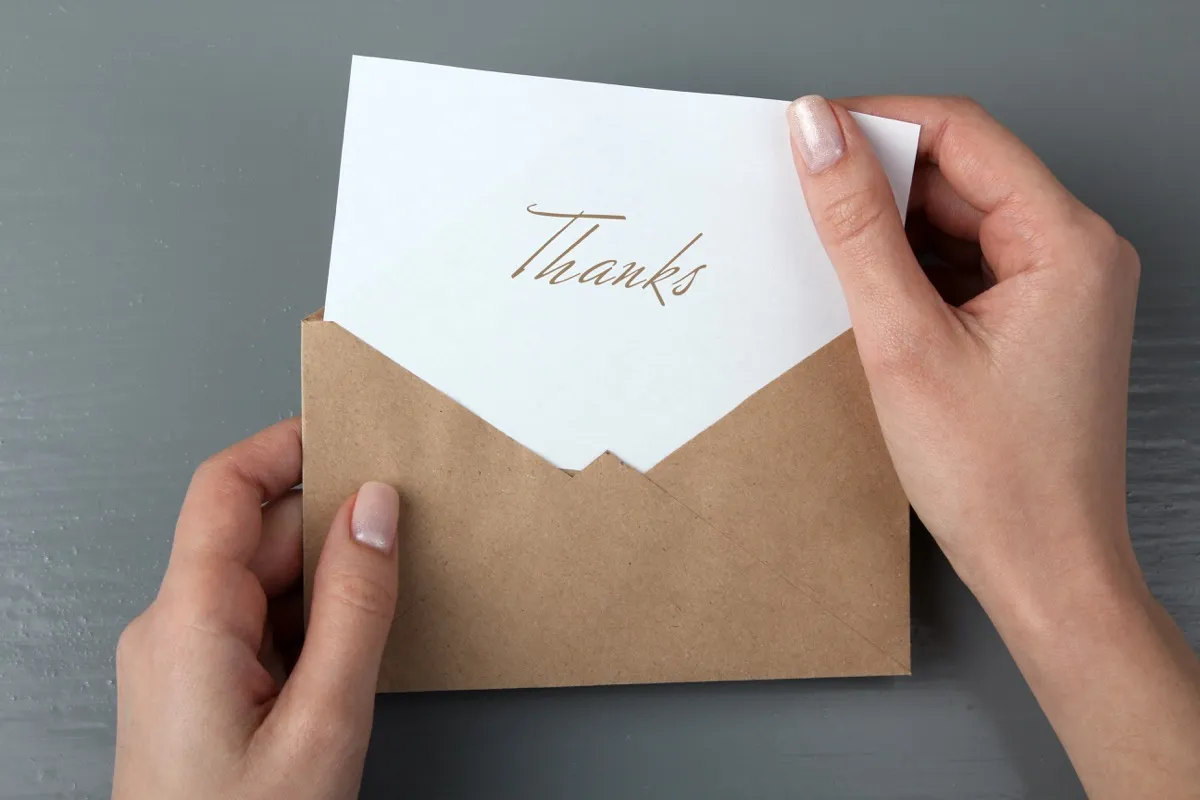 closeup of hands opening envelope to pull out a thank you note
