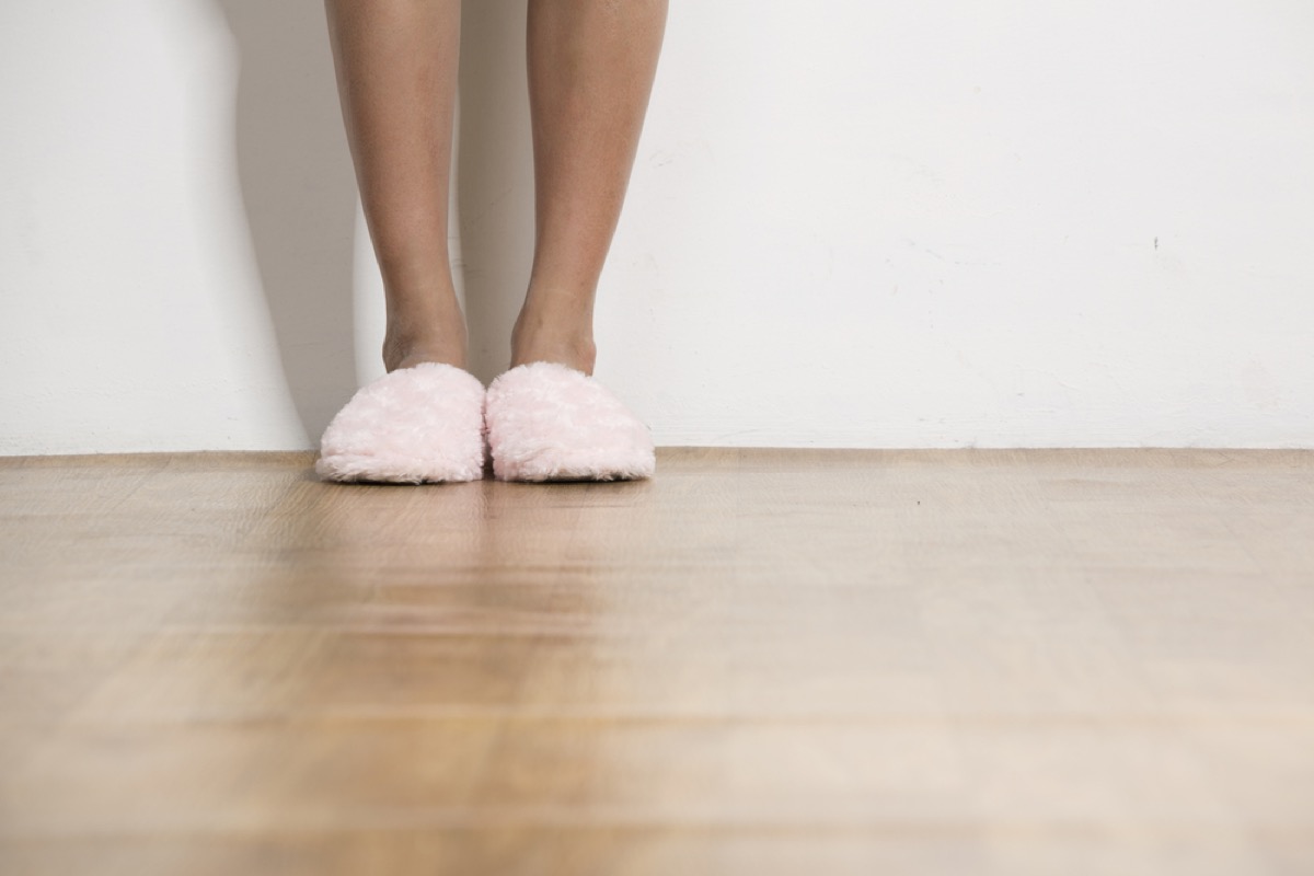 white woman's legs in pink slippers on wood floor