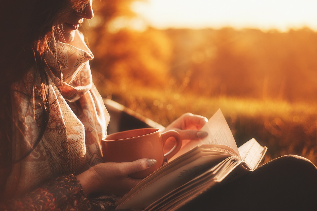 woman reading a book outside at sunset holding a cup, reducing alzheimer's risk