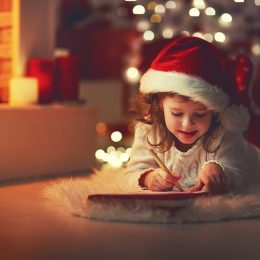 young child writing santa claus a letter in front of a christmas tree