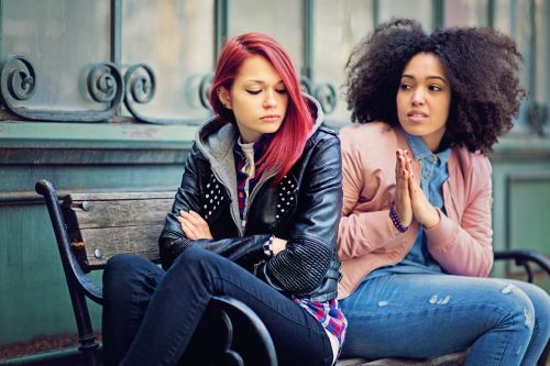 Lesbians in conflict are sulking on bench while one begs the older