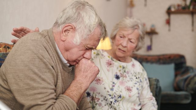 senior man with wife at home coughing badly, signs your cold is more serious