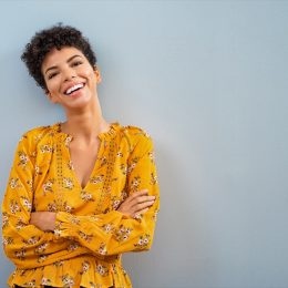 Portrait of beautiful cheerful girl smiling and looking at camera. Happy african woman in casual standing on blue background. Brazilian stylish woman with crossed arms and curly hair isolated with copy space.