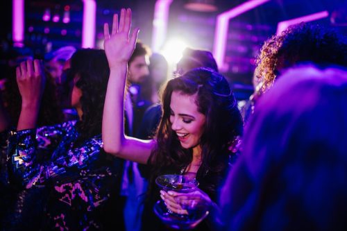 happy young adult woman dancing with her friends in a night club holding a cocktail in hand
