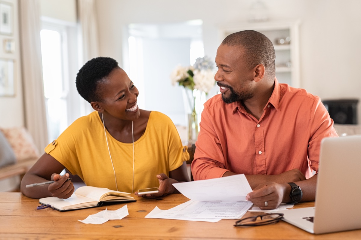 Cheerful mature couple sitting and managing expenses at home. Happy african man and woman paying bills together and managing budget. Black smiling couple checking accountancy and bills while looking at each other.