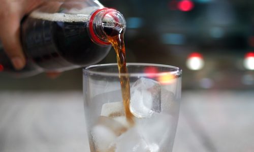 close up of cola being poured into glass filled with ice