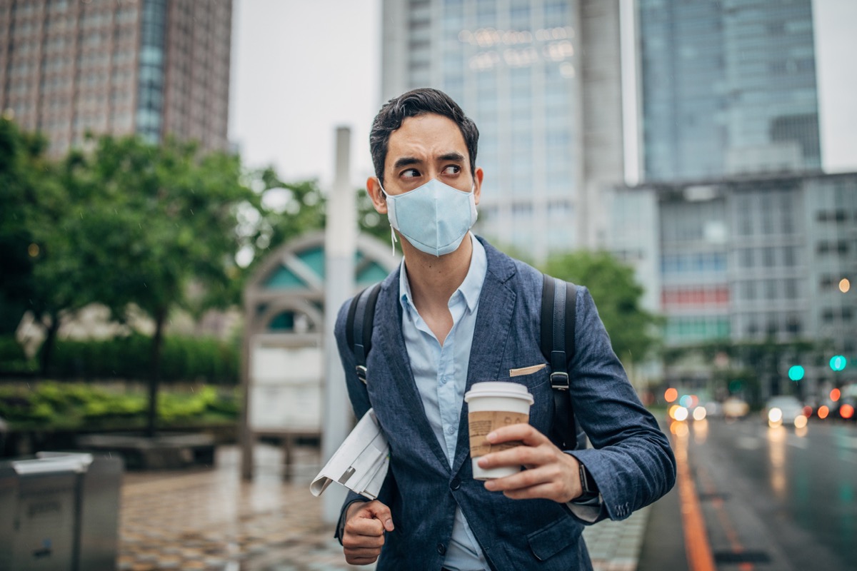 man in suit holding newspaper and coffee and wearing a face mask in city