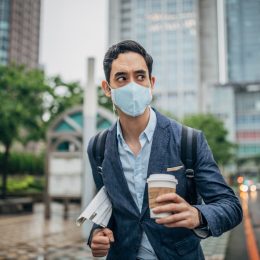 man in suit holding newspaper and coffee and wearing a face mask in city