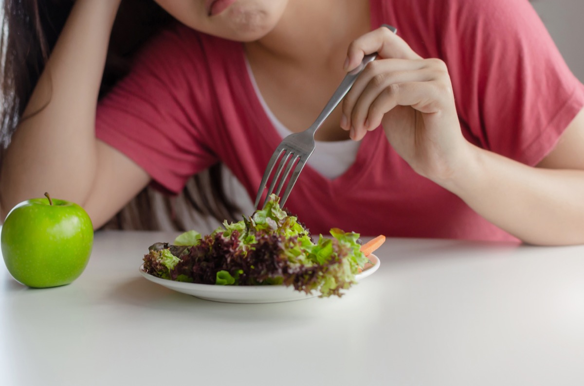 close up of young asian woman's frown as she picks at a salad with her fork